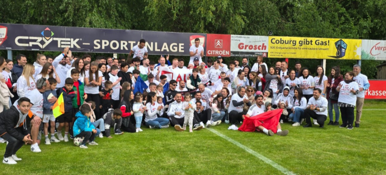Spieler, Familien und Fans des SV Bosporus Coburg versammeln sich gemeinsam auf dem Spielfeld zur Aufstiegsfeier.