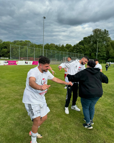 Spieler des SV Bosporus Coburg tanzen und feiern mit Fans nach dem Aufstieg auf dem Fußballplatz.