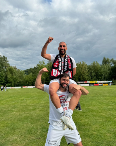 Zwei Fußballspieler des SV Bosporus Coburg feiern auf dem Spielfeld; einer sitzt jubelnd auf den Schultern des anderen.