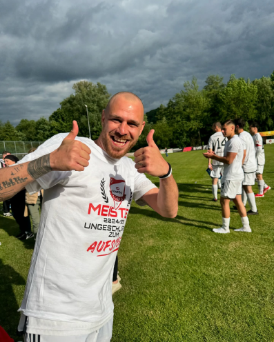 Lächelnder Fußballspieler mit Meister-T-Shirt zeigt beide Daumen hoch nach dem Aufstieg des SV Bosporus Coburg.